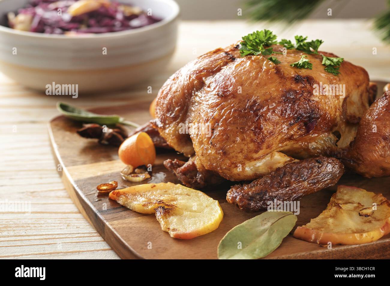 Festliches gebratenes Huhn frisch aus dem Ofen mit Äpfeln, Kumquat, Gewürzen und Kräutern serviert mit Rotkohl auf einem Holztisch, Geflügelessen zu Weihnachten Stockfoto