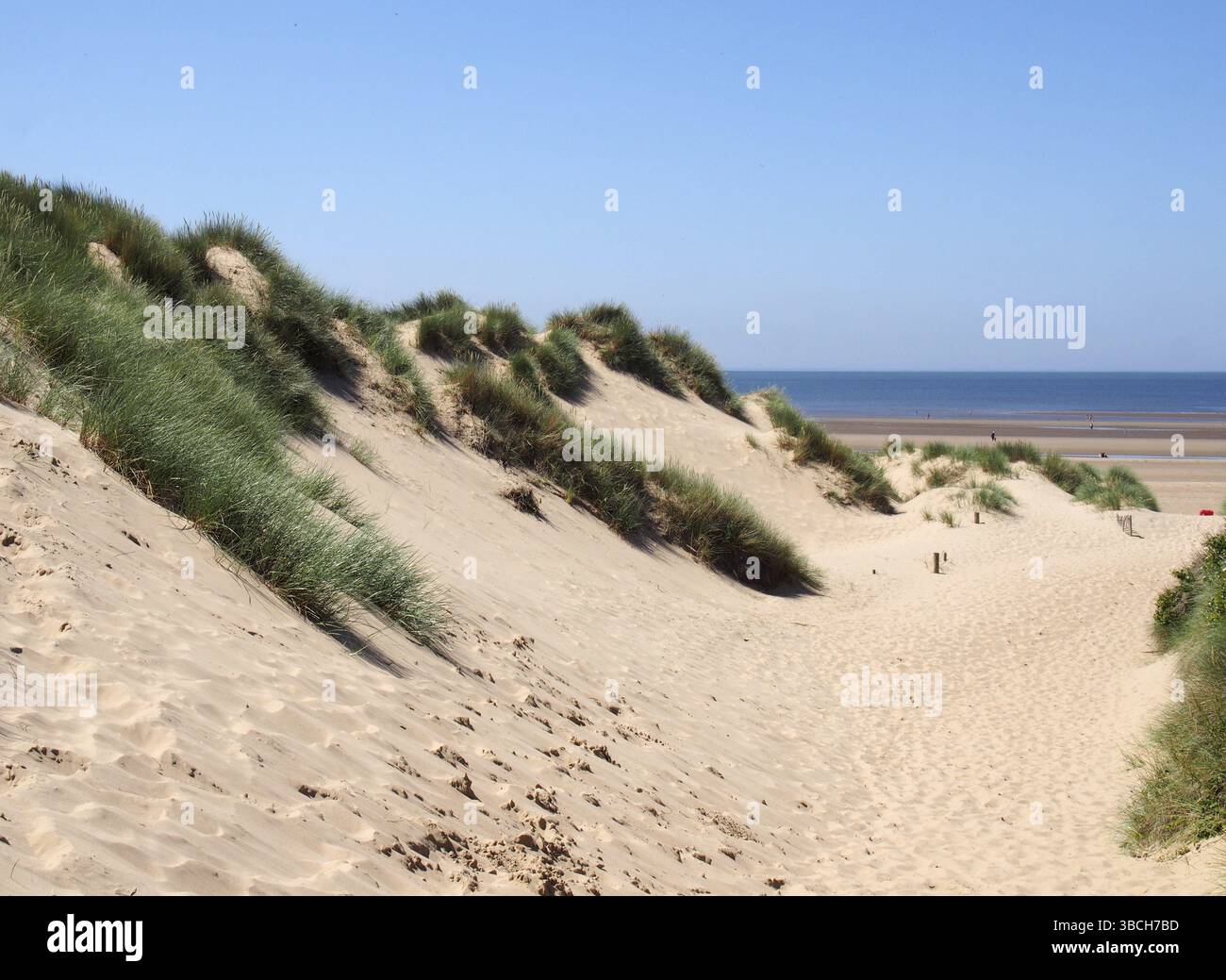 Ein Pfad durch hohe, mit Gras bedeckte Sanddünen, der zu einem Strand und dem hellblauen Meer im Sommersonnenlicht an der Küste von sefton in merseyside führt Stockfoto
