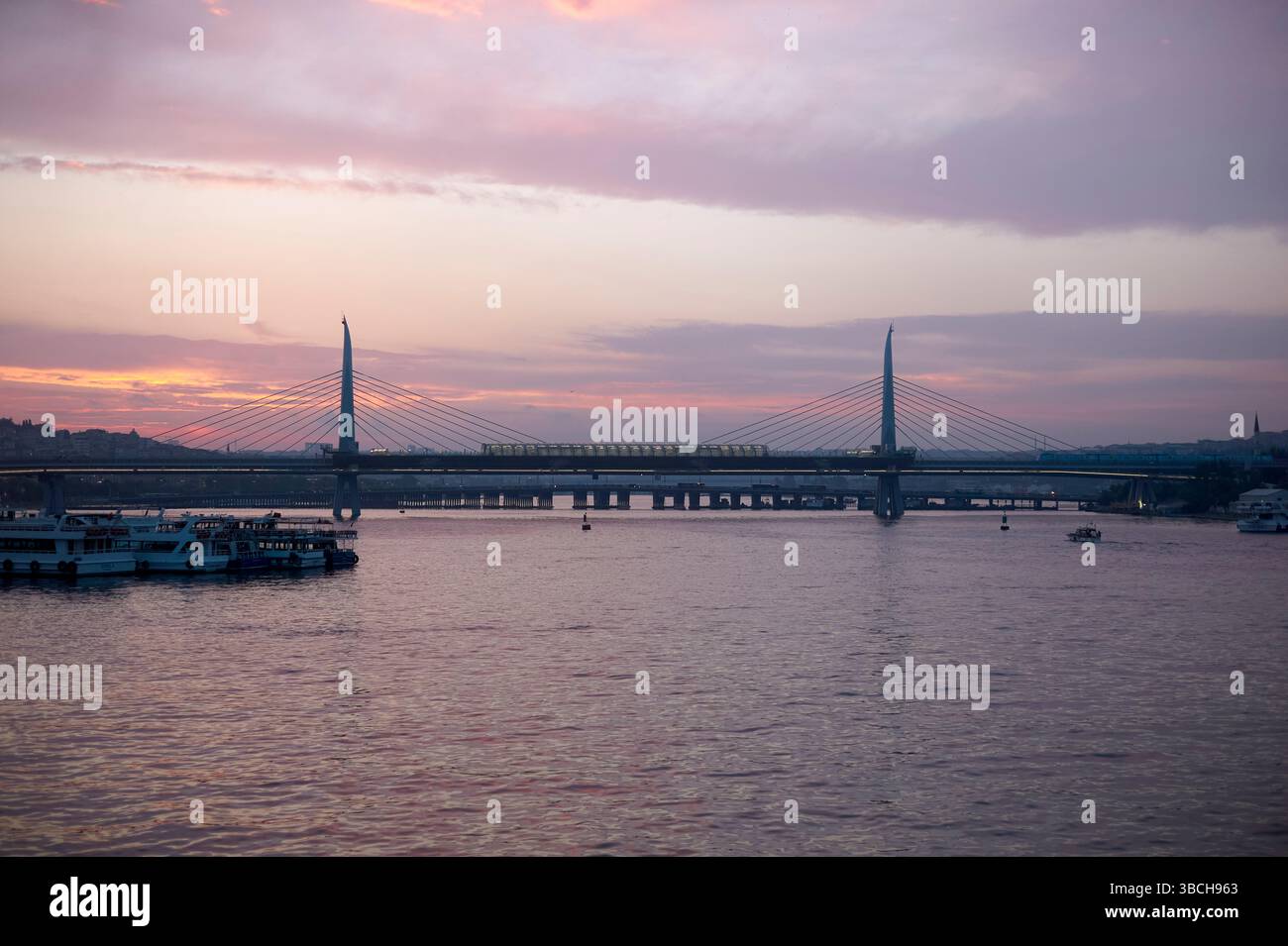 Blick bei Sonnenuntergang auf die Halic Metro Bridge oder Golden Horn Metro Bridge, über das Goldene Horn mit Booten und einem farbenfrohen Himmel. Istanbul, Türkei Stockfoto