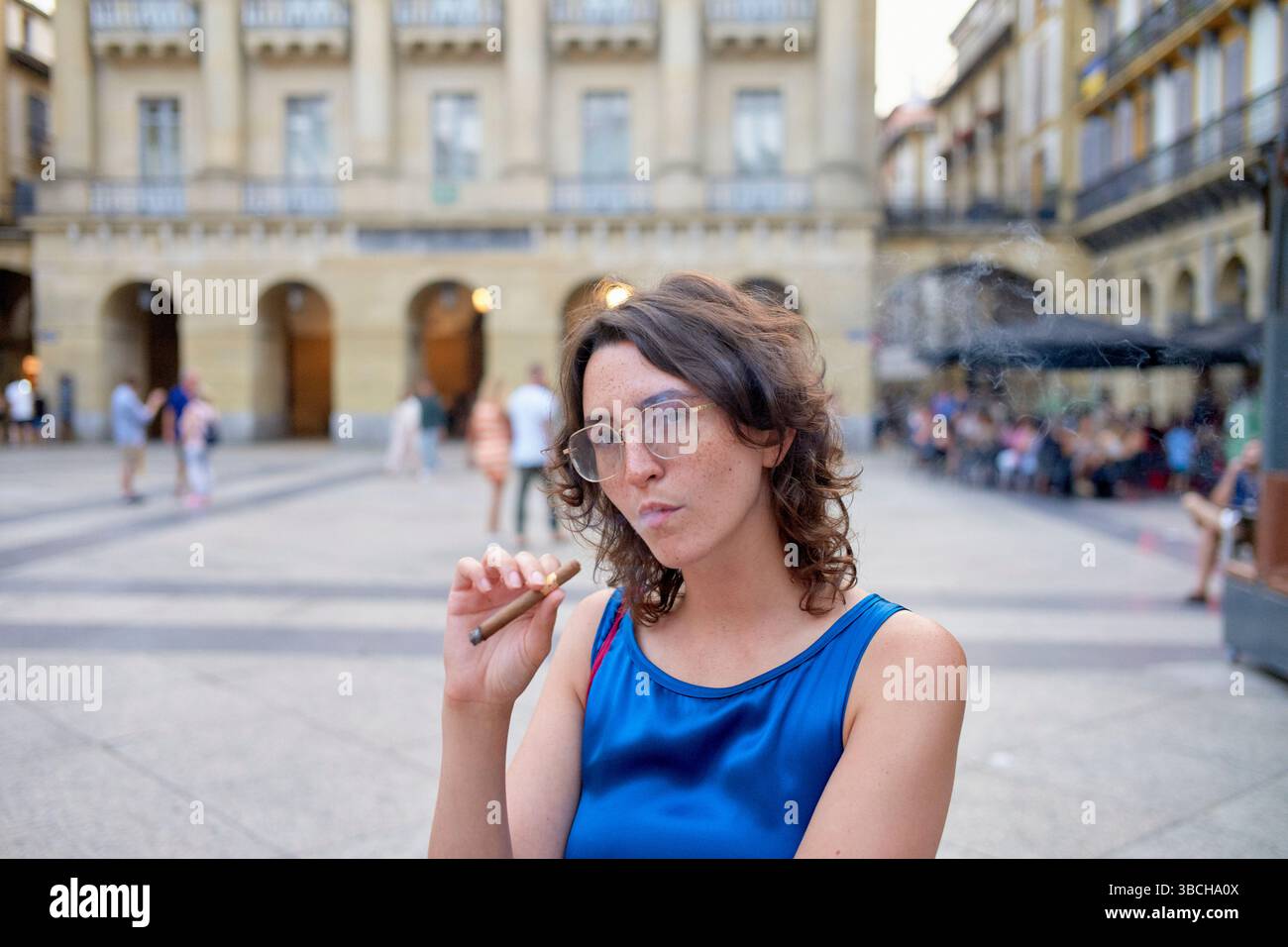 Frau in blauem Kleid raucht auf einem platz, umgeben von historischer Architektur. Stockfoto