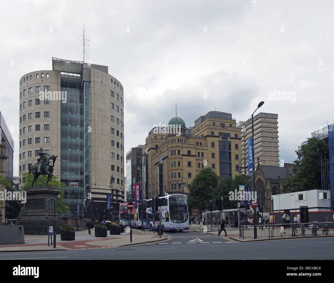 Leeds, West yorkshire, vereinigtes Königreich, 18. juni 2019: Busse und Fußgänger überqueren die Straße auf dem Stadtplatz leeds mit hohen Bürogebäuden im Park R. Stockfoto