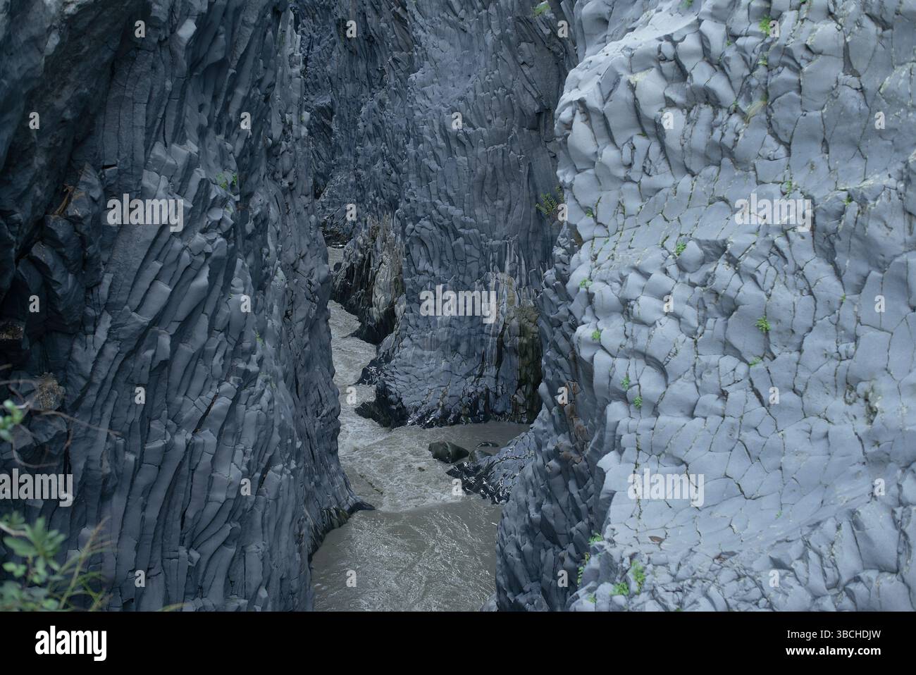 Schmale Schlucht mit schroffen grauen Felsformationen und einem turbulenten Fluss darunter. Sizilien, Italien Stockfoto