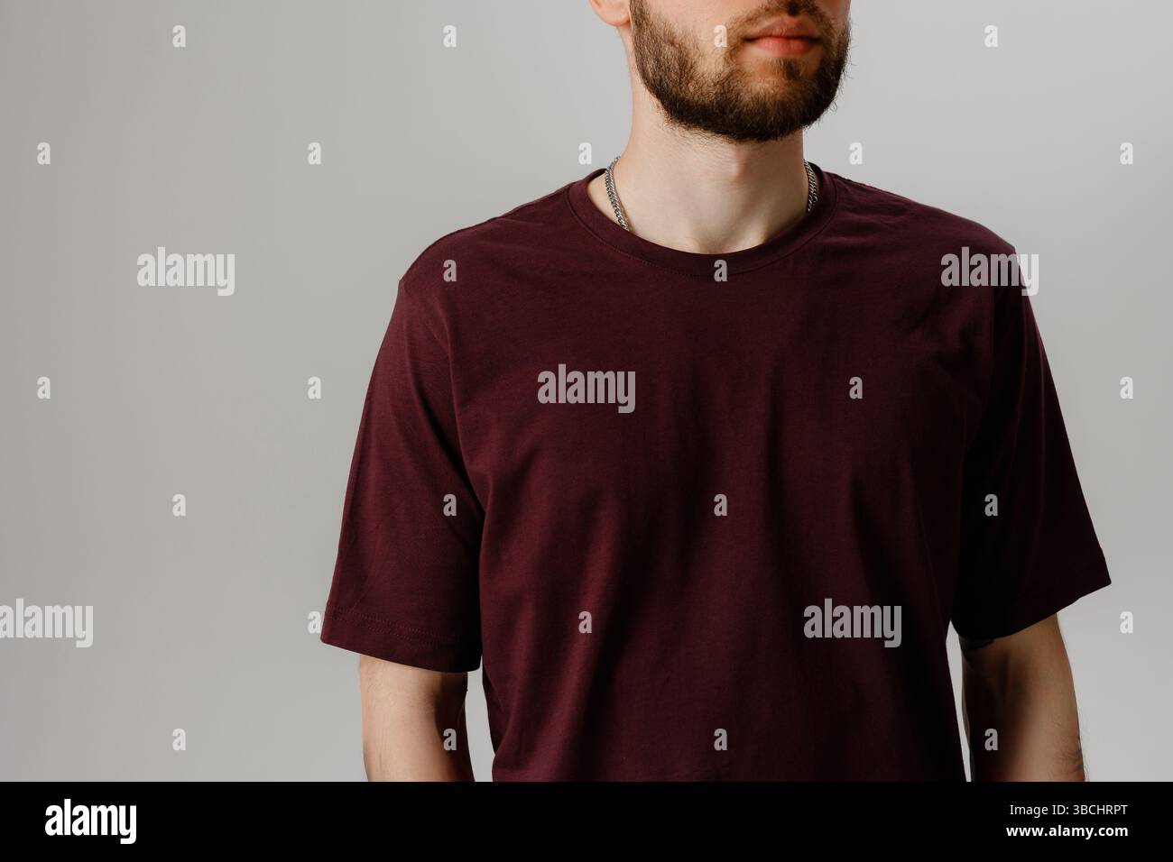 Lässiges Männermodell mit einem burgunderroten T-Shirt vor einem schlichten grauen Hintergrund während eines Fotoshootings im Studio Stockfoto