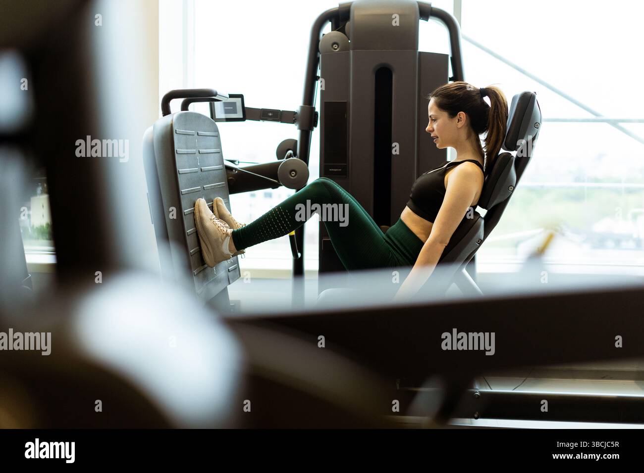 Ein engagierter Athlet nimmt an einer Beindruckübung Teil und zeigt während des Tages Entschlossenheit und Kraft in einer gut beleuchteten Fitnessumgebung. Stockfoto