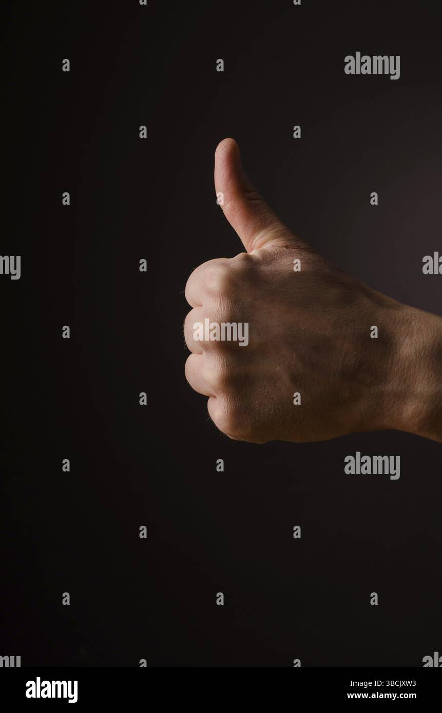 Männliche Hand mit Daumen oben auf einem dunklen Hintergrund Stockfoto