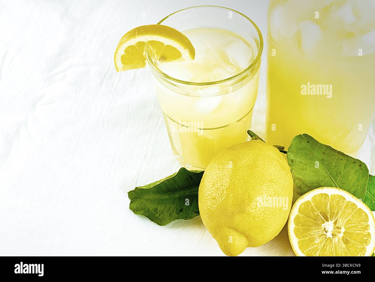 Frische organische Limonade in ein Glas mit Zitronen und Blätter und ein Glas Limonade auf einen weißen Hintergrund mit Kopie Raum Stockfoto