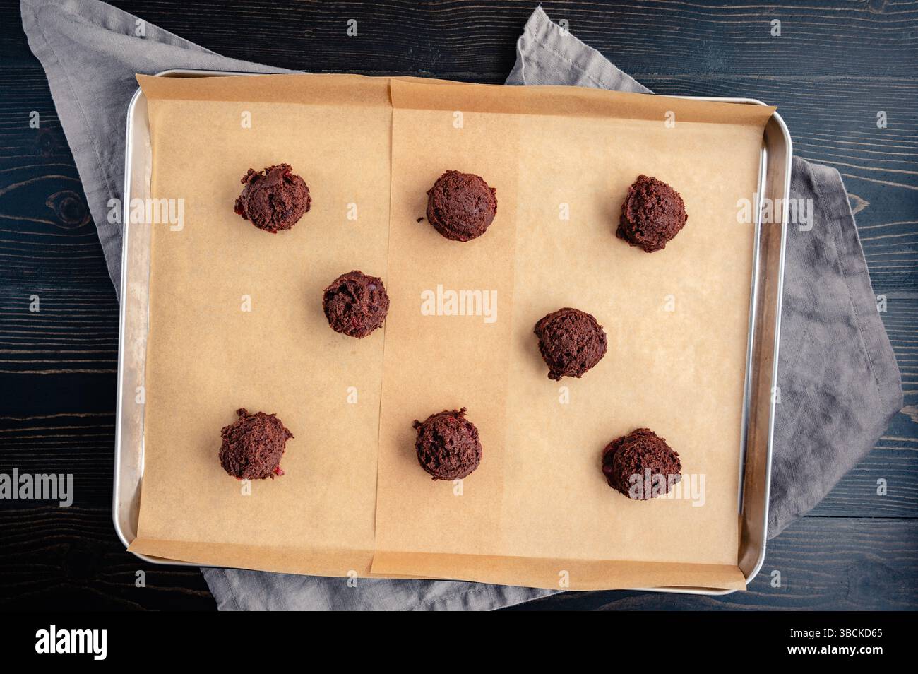 Acht Kugeln Schokolade-Kirschkekse-Teig auf Blatt-Pfanne: Kugeln mit gekühltem Keksenteig, die auf einem mit Backpapier ausgelegten Backblech verteilt sind Stockfoto