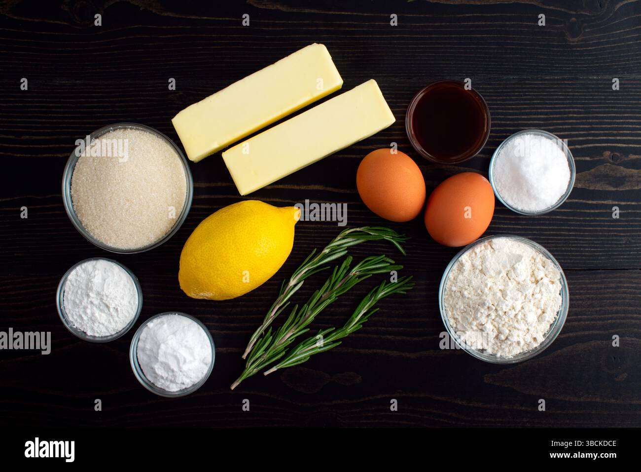 Rosmarin-Zitronenzucker Cookies Zutaten: Mehl, Butter, Zucker, Eier und andere Kekszutaten auf einem dunklen Holztisch Stockfoto