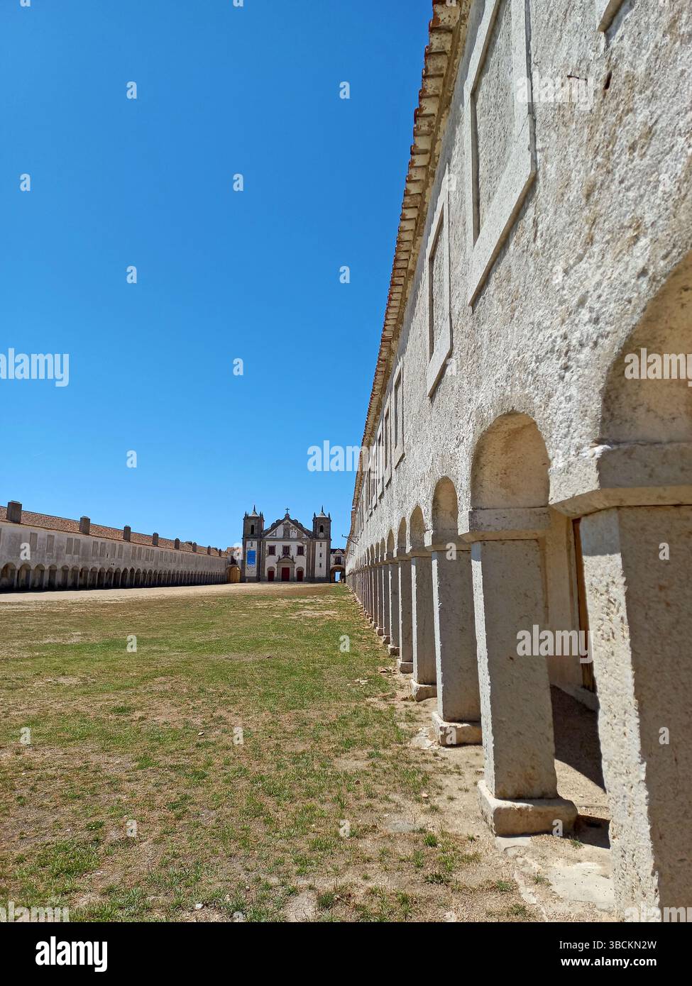 Altes religiöses Heiligtum am Kap Espichel in Sesimbra Portugal mit langen symmetrischen Arkaden und einer historischen Kirchenfassade unter einem leuchtenden Blau Stockfoto