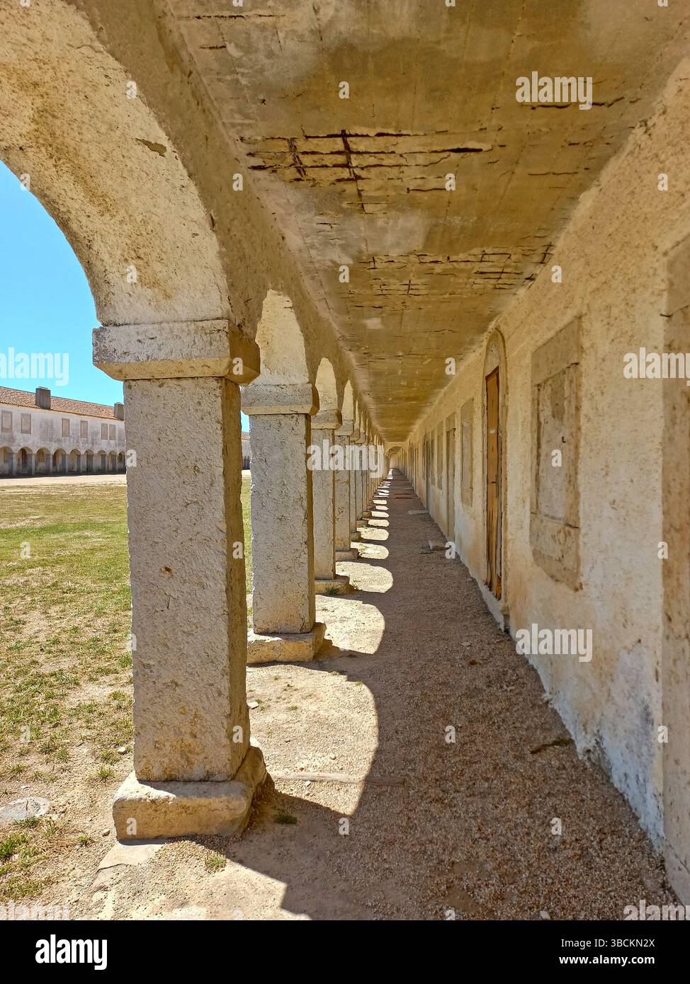 Altes religiöses Heiligtum am Kap Espichel in Sesimbra Portugal mit langen symmetrischen Arkaden und einer historischen Kirchenfassade unter einem leuchtenden Blau Stockfoto