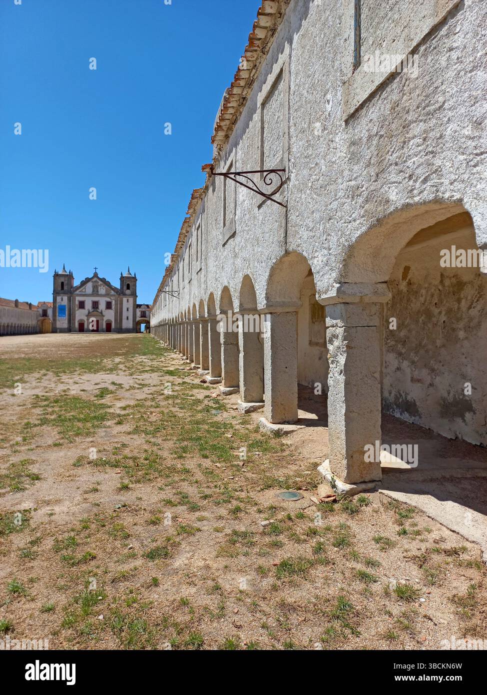 Altes religiöses Heiligtum am Kap Espichel in Sesimbra Portugal mit langen symmetrischen Arkaden und einer historischen Kirchenfassade unter einem leuchtenden Blau Stockfoto