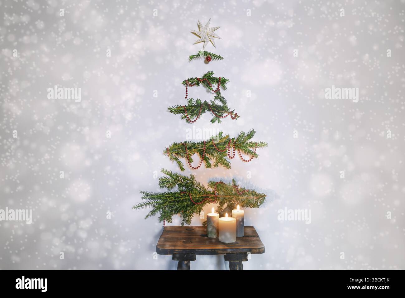 Weihnachtsbaumalternative, immergrüne Zweige mit Dekoration, die an der Wand über einem rustikalen Holzhocker mit Kerzen hängen, nachhaltige Feiertage Agave Stockfoto