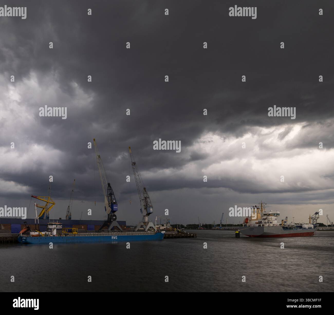 Frachtschiffe und Kräne am Hafen von Rotterdam, Niederlande, unter einem dramatischen Sturmhimmel. Stockfoto