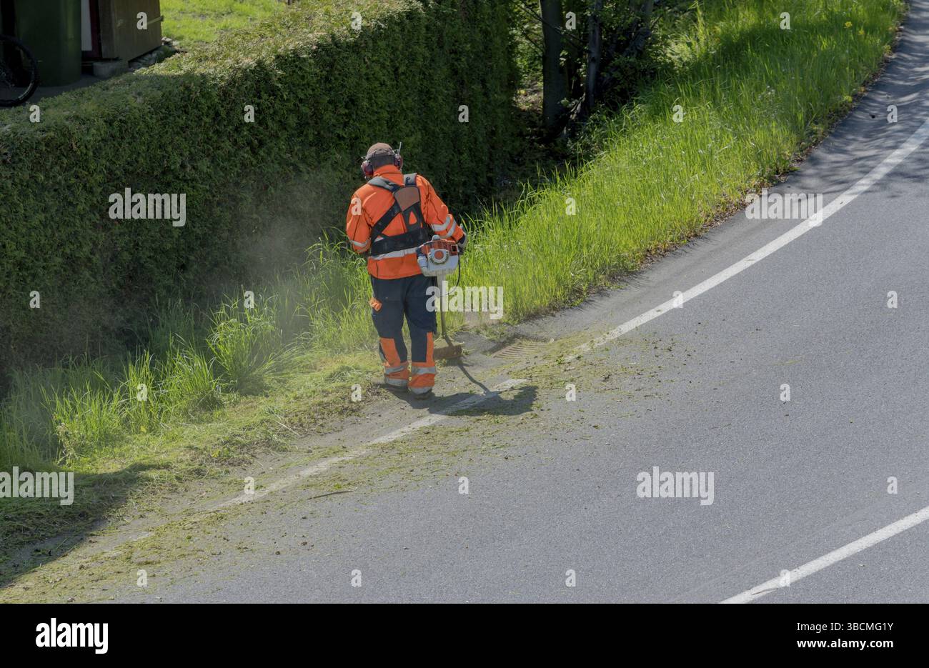 Ein stadtarbeiter Clearing am Straßenrand von Gras und Unkraut mit einem weed Eater Stockfoto