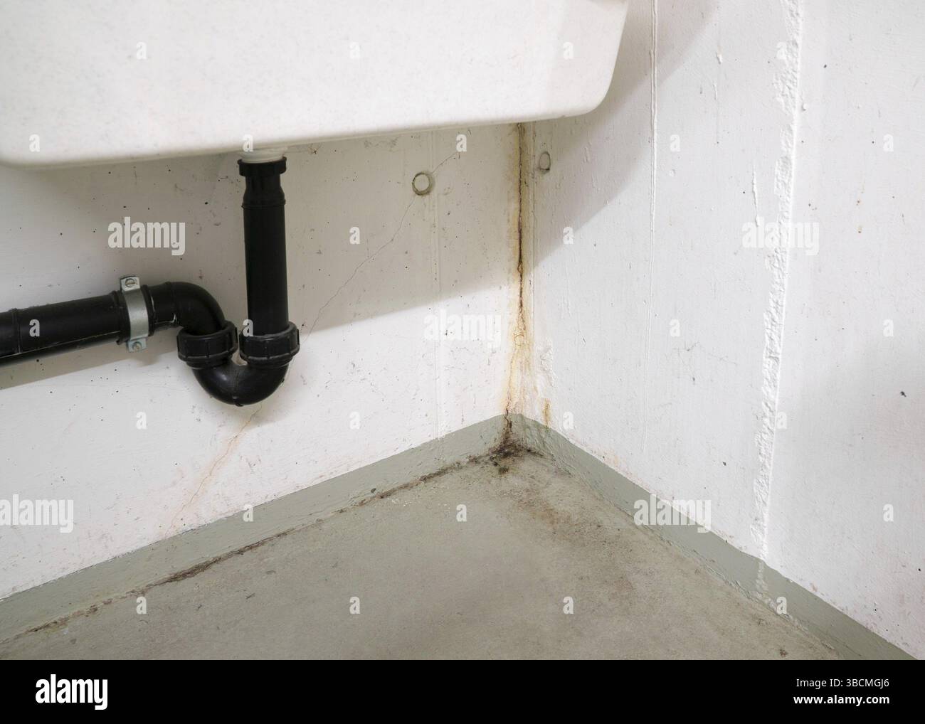 Oxidiert und verrostet Kalzium- und Schimmel- und Mehltaupilzen Einlagen von Wasserschäden in einem konkreten Keller unter einem großen weißen Waschbecken im Detail Stockfoto