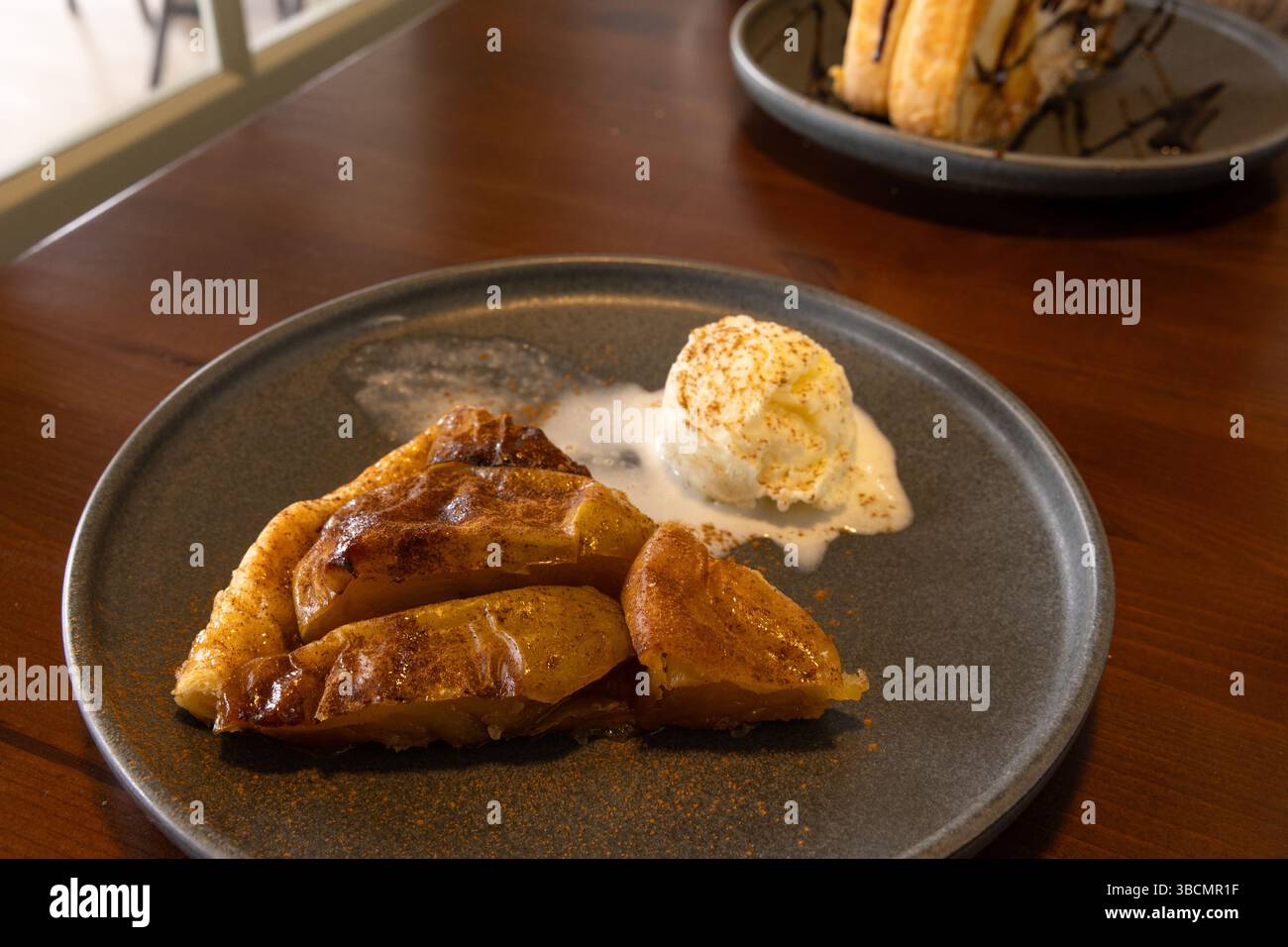 Selektiver Fokus auf Apfelkuchen mit Zimt bestreut, serviert mit Eiskugel auf einem Teller. Mit Apfelhälften auf Blätterteig gemacht. Stockfoto