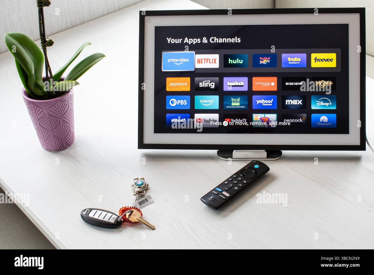 San Francisco, KALIFORNIEN, 20. Mai 2025: Amazon Echo Show zeigt App-Symbole auf weißem Tisch mit Fire TV Fernbedienung, Orchidee und Tasten in einem Smart Home Setup. Stockfoto