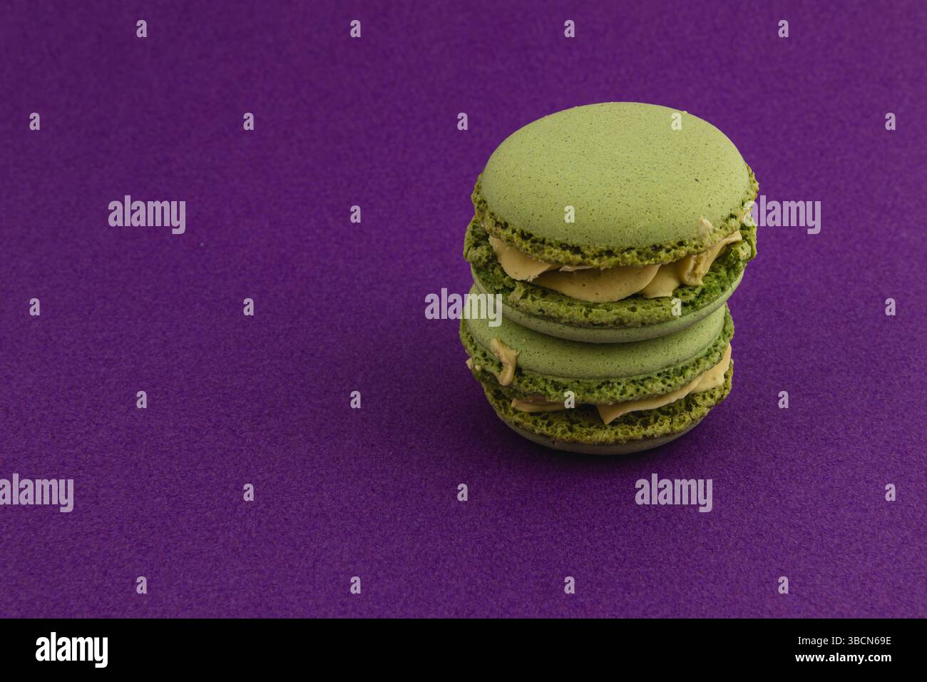 Zwei Matcha-Macarons mit cremiger Mitte sind auf einem leuchtend violetten Hintergrund gestapelt und zeigen ihre glatte Textur und ansprechende grüne Farbe. Stockfoto