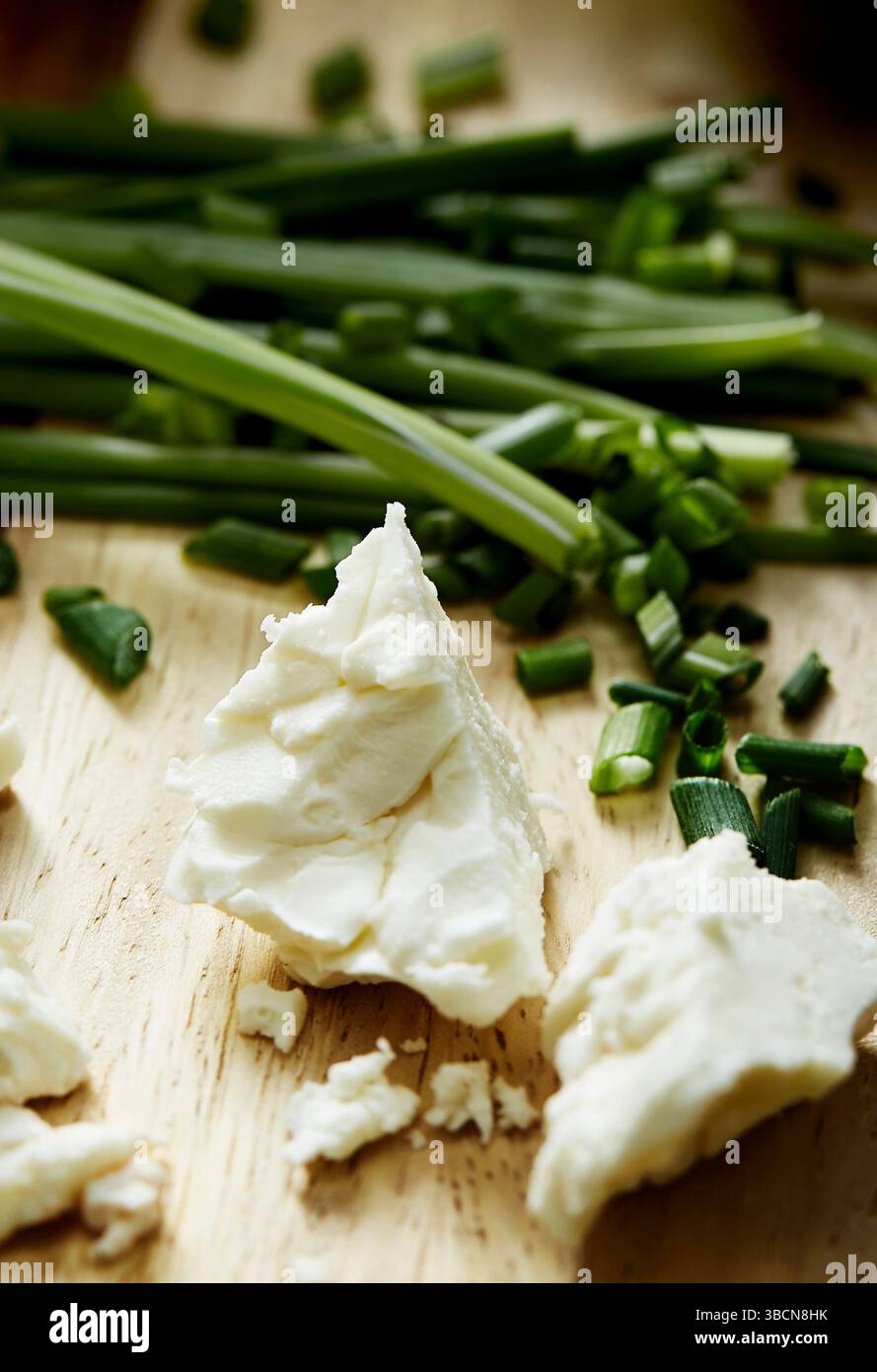 Zerbröckelter Weißkäse mit Schnittlauch auf Holzbrett Stockfoto