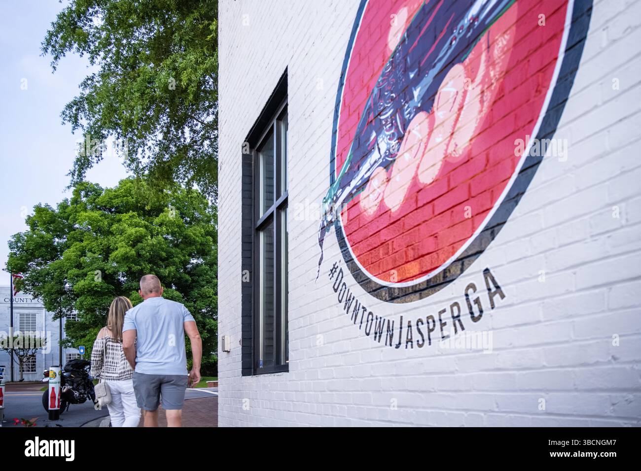Ein Paar, das in der Abenddämmerung an einem Wandgemälde von Coca-Cola in der Innenstadt von Jasper, Georgia vorbeiläuft. (USA) Stockfoto