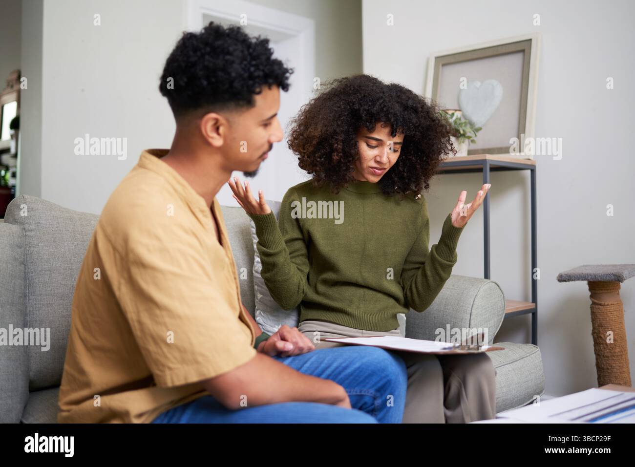 Ein paar diskutieren über Finanzpapiere auf Sofa zu Hause in Casual Clothing Stockfoto