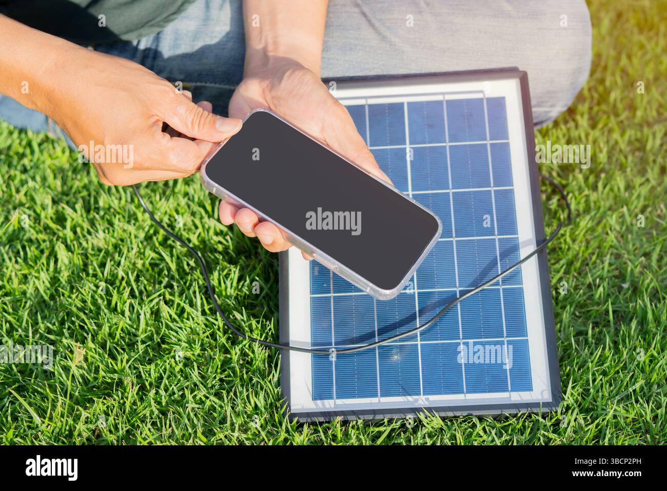 Nicht erkennbare Person, die die Solarmodule zum Aufladen eines Smartphones im Freien nutzt. Energiekonzept. Stockfoto