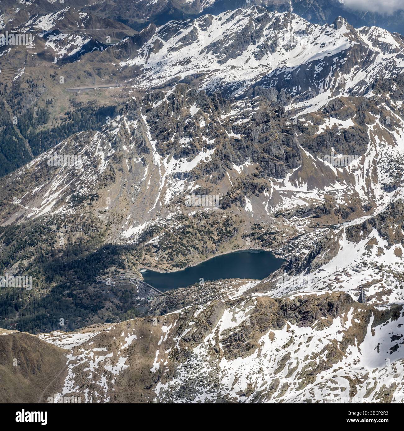 Luftlandschaft mit Trona-Staudamm und Stausee auf der Nordseite des Tre Signori-Gipfels, aufgenommen von einem Segelflugzeug in hellem Frühlingslicht, ne Stockfoto