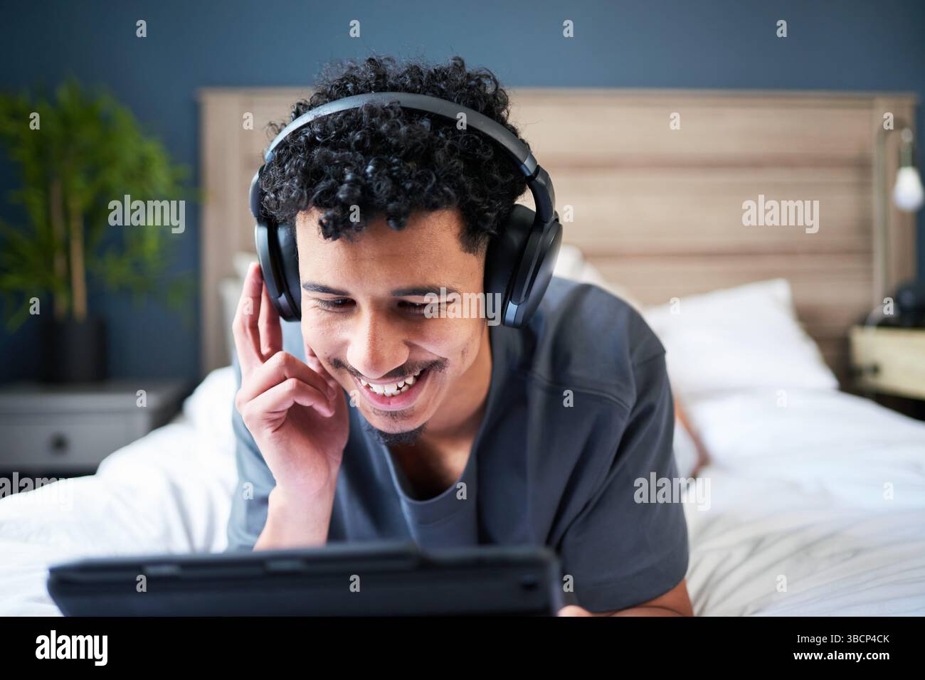 Glücklicher junger Mann, der Musik über Kopfhörer genießt, während er sich auf einem Bett zu Hause entspannt Stockfoto