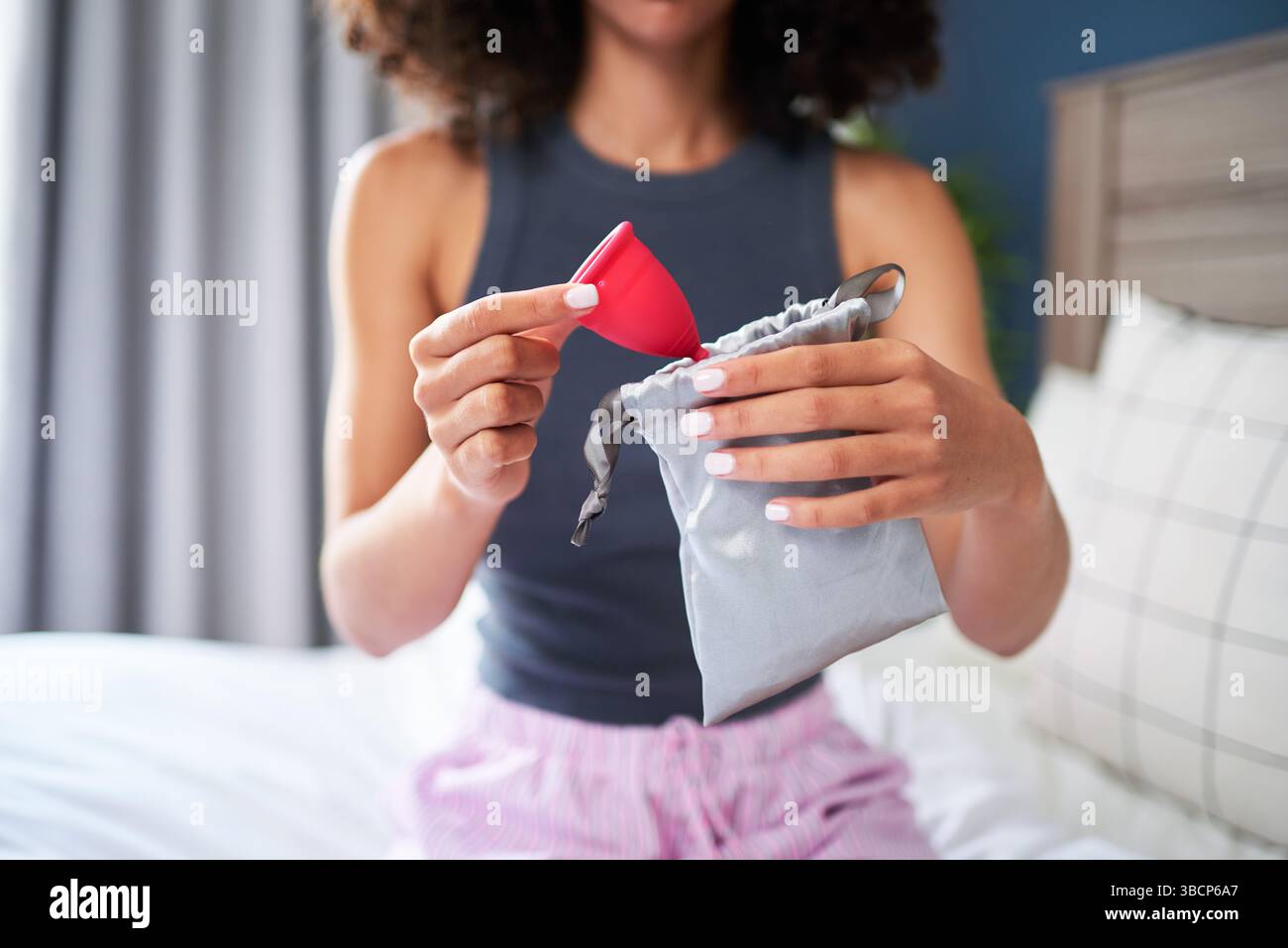 Junge Frau, die einen Menstruationsbecher mit Aufbewahrungsbeutel in einem komfortablen Zuhause hält Stockfoto