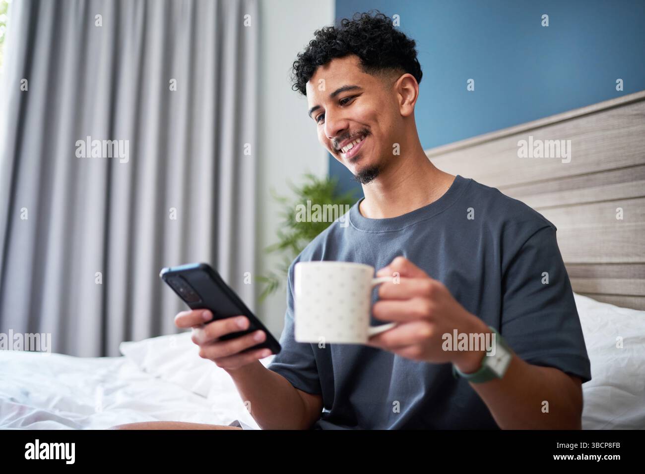 Mann genießt Morgenkaffee, während er sich mit dem Smartphone in komfortabler Wohnumgebung einlässt Stockfoto