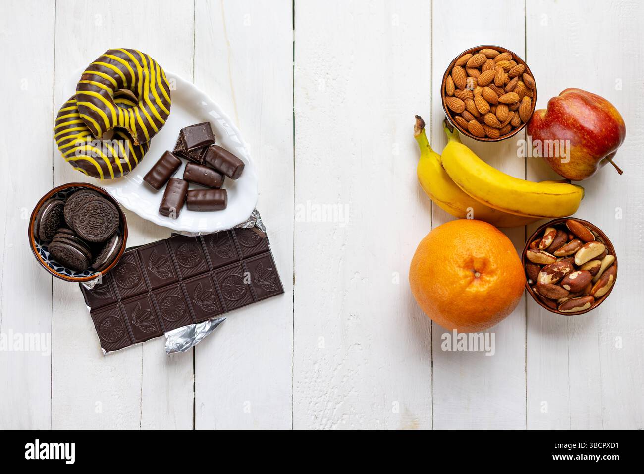 Gesunde und ungesunde Lebensmittel-Entscheidungen Vergleich. Blick von oben auf gesunde Früchte und Nüsse im Kontrast zu zuckerhaltiger Schokolade, Keksen und Donuts auf einem weiß Stockfoto
