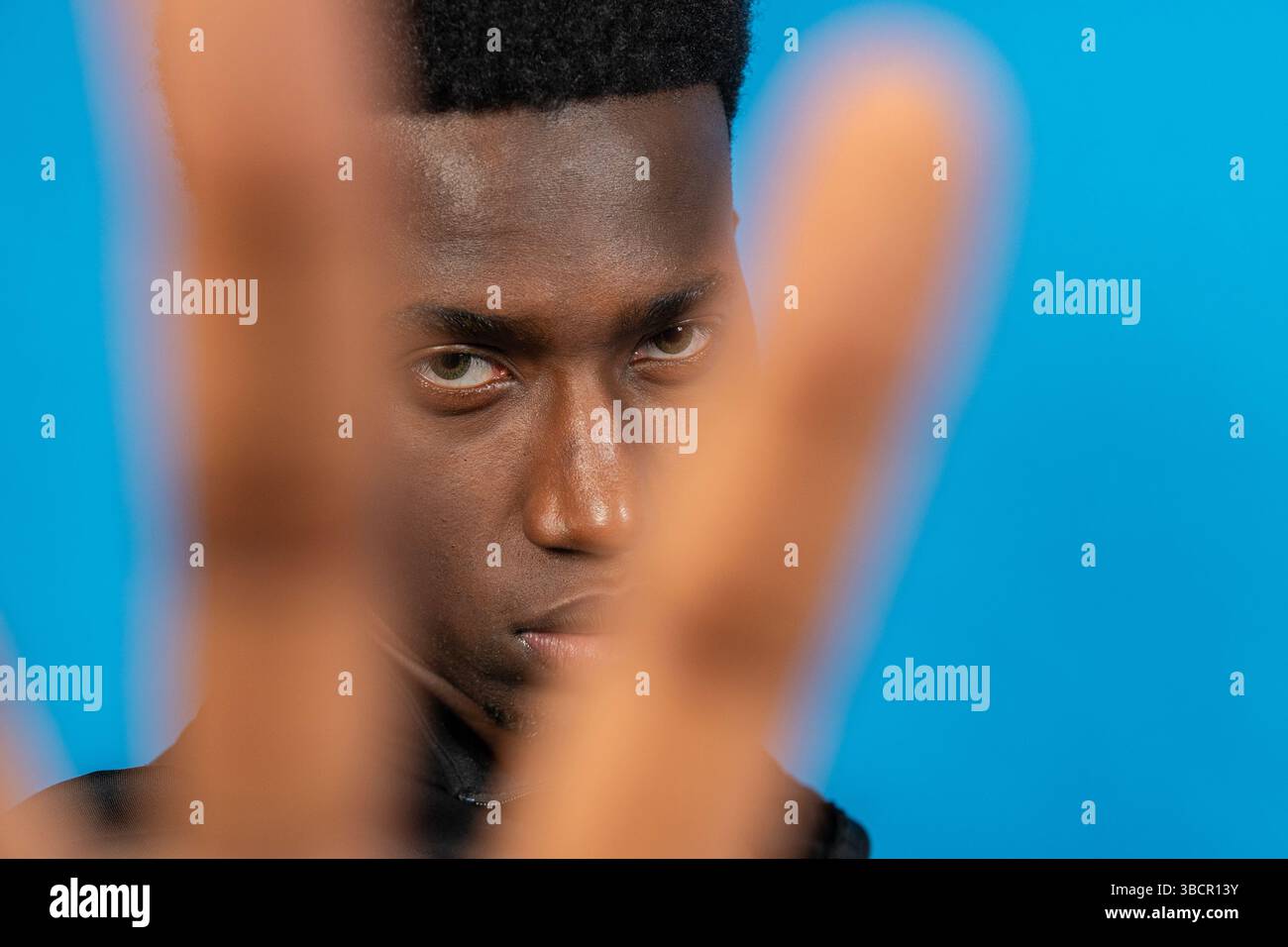 Nahporträt eines ernsten jungen Mannes, der mit seiner Hand vor einem leuchtend blauen Hintergrund aufhört Stockfoto