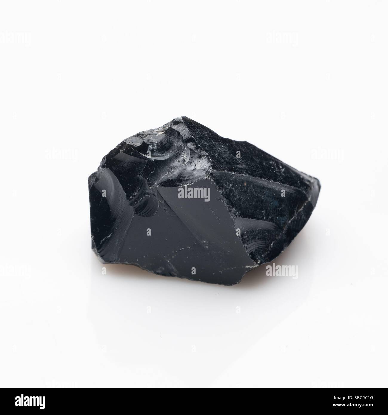 Ein roher, dunkler, glänzend schwarzer Obsidian-Gesteinsfragment mit internen Strömungsmustern und subtilen grauen Einschlüssen, die einen Glaskörper und scharfe Kanten zeigen. Stockfoto
