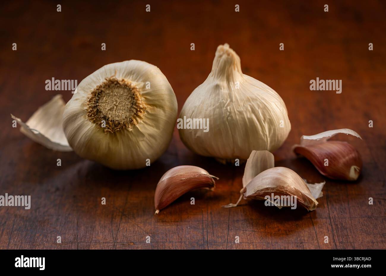 Ganzer und geschälter roher Knoblauch auf hölzernem Schneidebrett Stockfoto