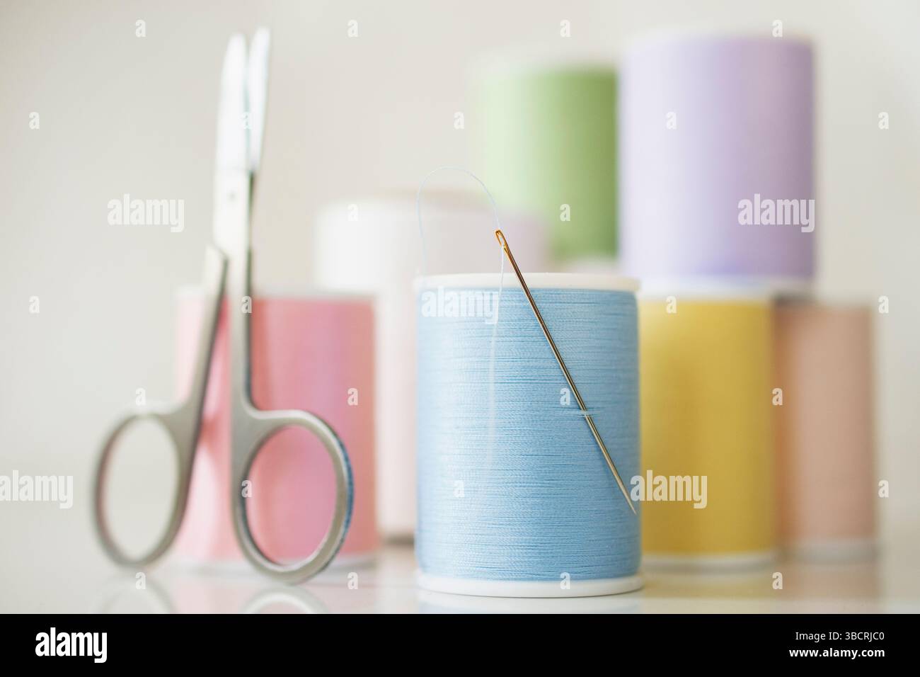 Studio-Aufnahme mit Spulen aus pastellfarbenem Garn, Nadel und Schere Stockfoto