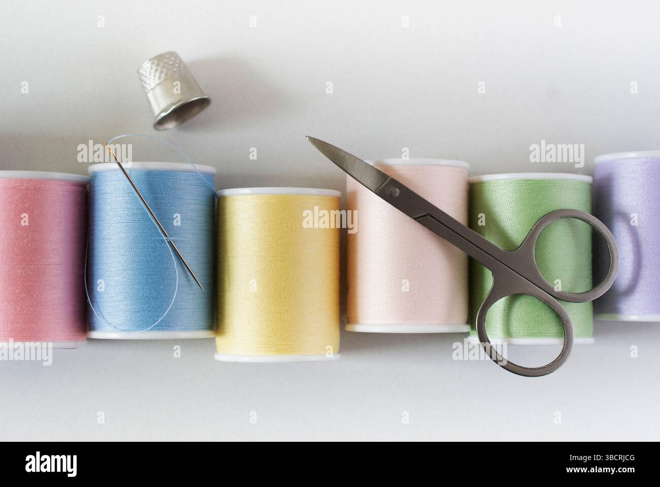 Studio-Aufnahme mit Spulen aus pastellfarbenem Garn, Nadel, Fingerhut und Schere Stockfoto