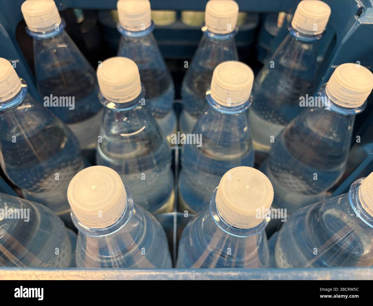 Mehrere Flaschen mit klarem Wasser sind in einer blauen Kunststoffkiste angeordnet, in der die Etiketten und Verschlüsse ausgestellt sind. Diese Einstellung empfiehlt die Vorbereitung auf eine m Stockfoto