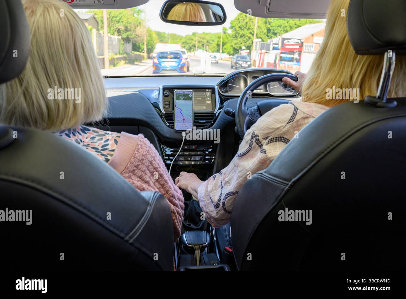 Rücksitzansicht von zwei Frauen auf den Vordersitzen eines Autos, Fahrer und Beifahrer, Blick durch die Windschutzscheibe. Stockfoto