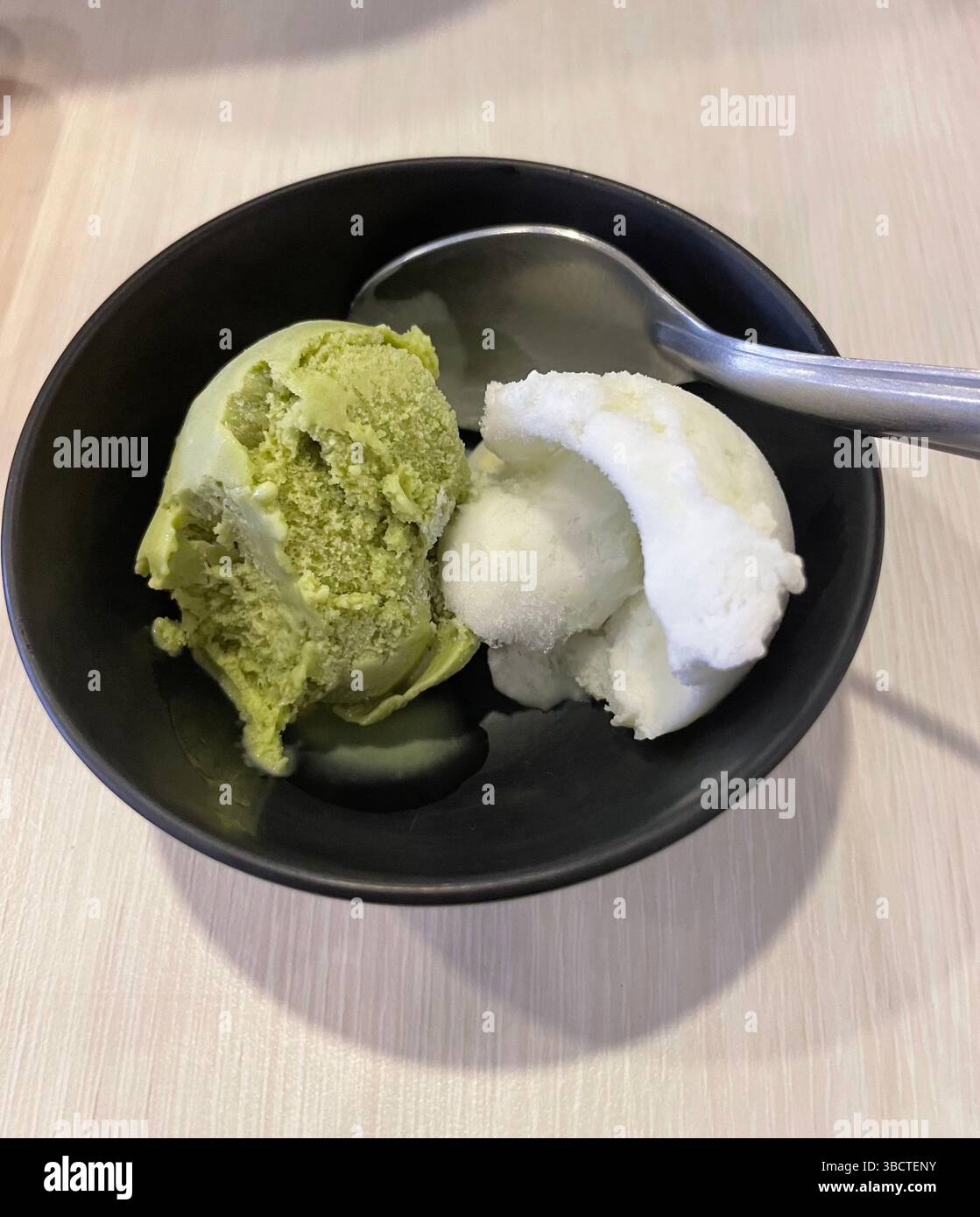 Erfrischende Schaufeln grüner Tee und Kokos-Eis in einer schwarzen Schüssel – eine unwiderstehliche Mischung aus cremiger Textur und exotischen Aromen bei jedem Happen. - Smartphone-aufgenommenes Stockfoto