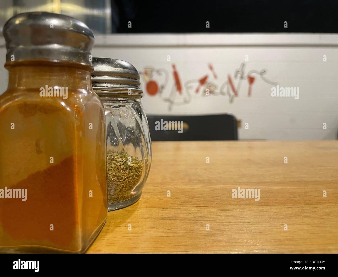 Zwei Gewürzgläser aus Glas ruhen auf einem rustikalen Holztisch, elegante Küchenutensilien, die jedem kulinarischen Raum Geschmack, Funktion und ästhetischen Charme verleihen. Stockfoto