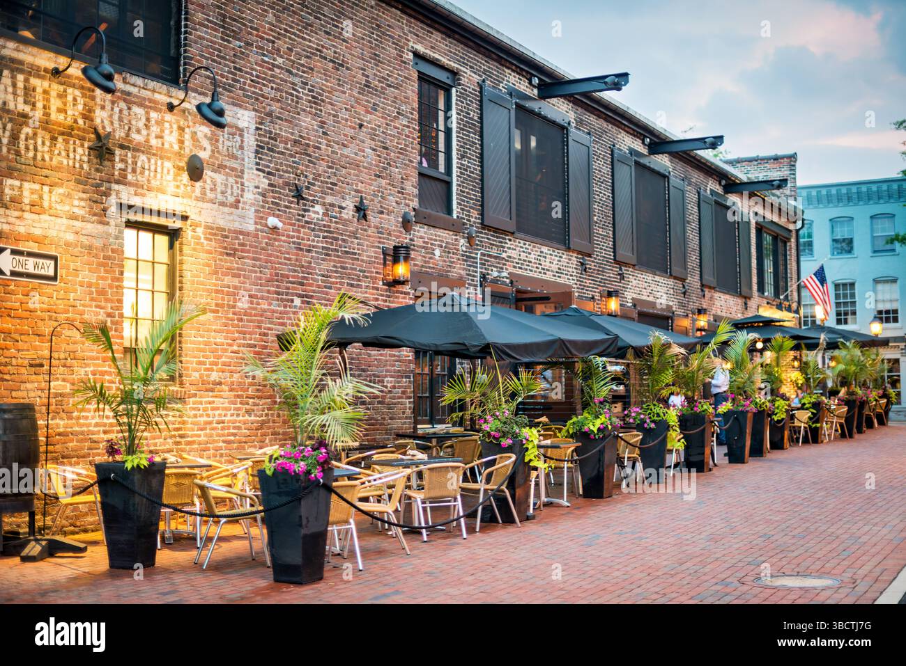 Virtue Feed and Grain Restaurant Outdoor Seating Alexandria Virginia // ALEXANDRIA, Virginia, Vereinigte Staaten – im Restaurant Virtue Feed and Grain können Sie im historischen Viertel der Altstadt von Alexandria im Freien speisen. Das Restaurant befindet sich in einem renovierten Lagerhaus aus dem 19. Jahrhundert, das einst als Futtermittel- und Getreidelager an der 106 South Union Street diente. Das Hotel liegt nur einen Block vom Potomac River Uferpromenade entfernt und bietet Gästen die Möglichkeit, Mahlzeiten zu genießen und gleichzeitig den historischen Charme der Altstadt von Alexandria zu erleben. Die Sitzplätze auf der Terrasse erweitern die Essenskapazität des Restaurants auf bis zu 10 Stockfoto