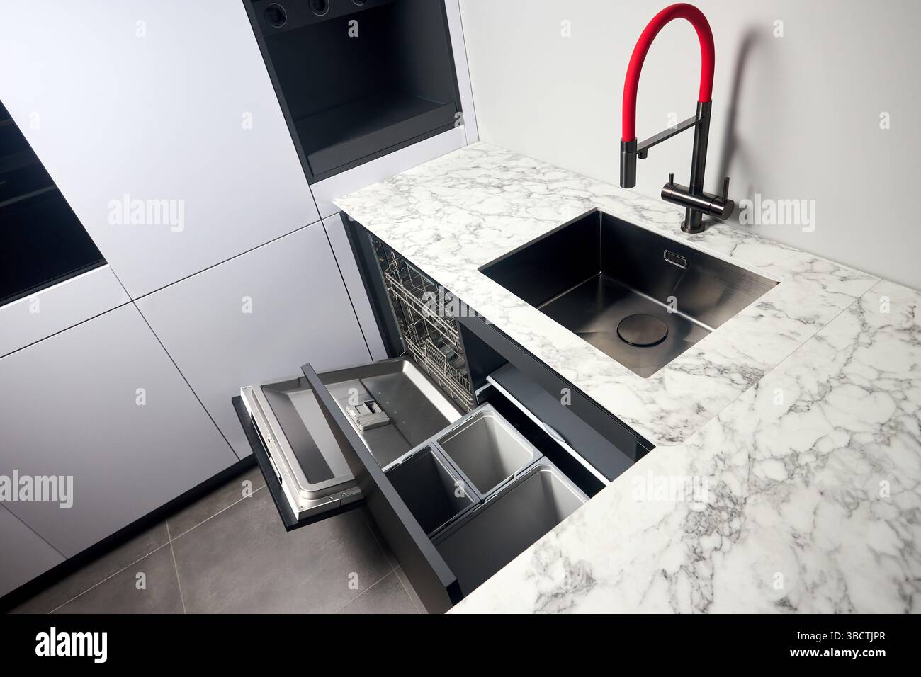 Küche mit eingebautem, geöffnetem Geschirrspüler und herausziehbarer Schublade für die getrennte Abfallsammlung. Wasserhahn Waschbecken mit kompaktem Hochdruck Stockfoto