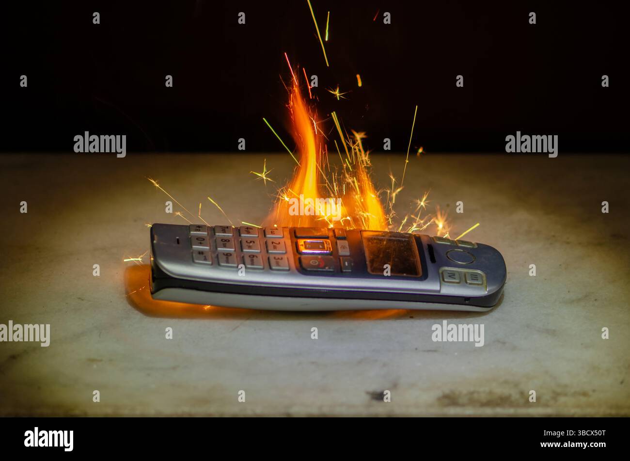 Ein brennendes Festnetztelefon mit Drucktasten und hellen Flammen und Funken ist ein Symbol für veraltete Technologie, Überhitzungsgefahr oder brennende Elektronik Stockfoto