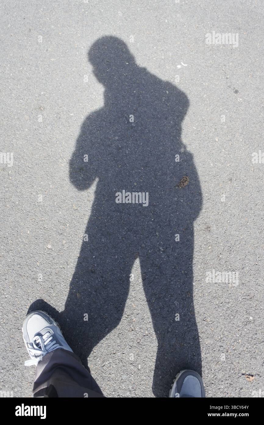 Der Schatten einer Person auf der Asphaltstraße, während des Tages, wenn die Sonne über der Straße ist, ist der Schatten seines ganzen Körpers sichtbar. Stockfoto