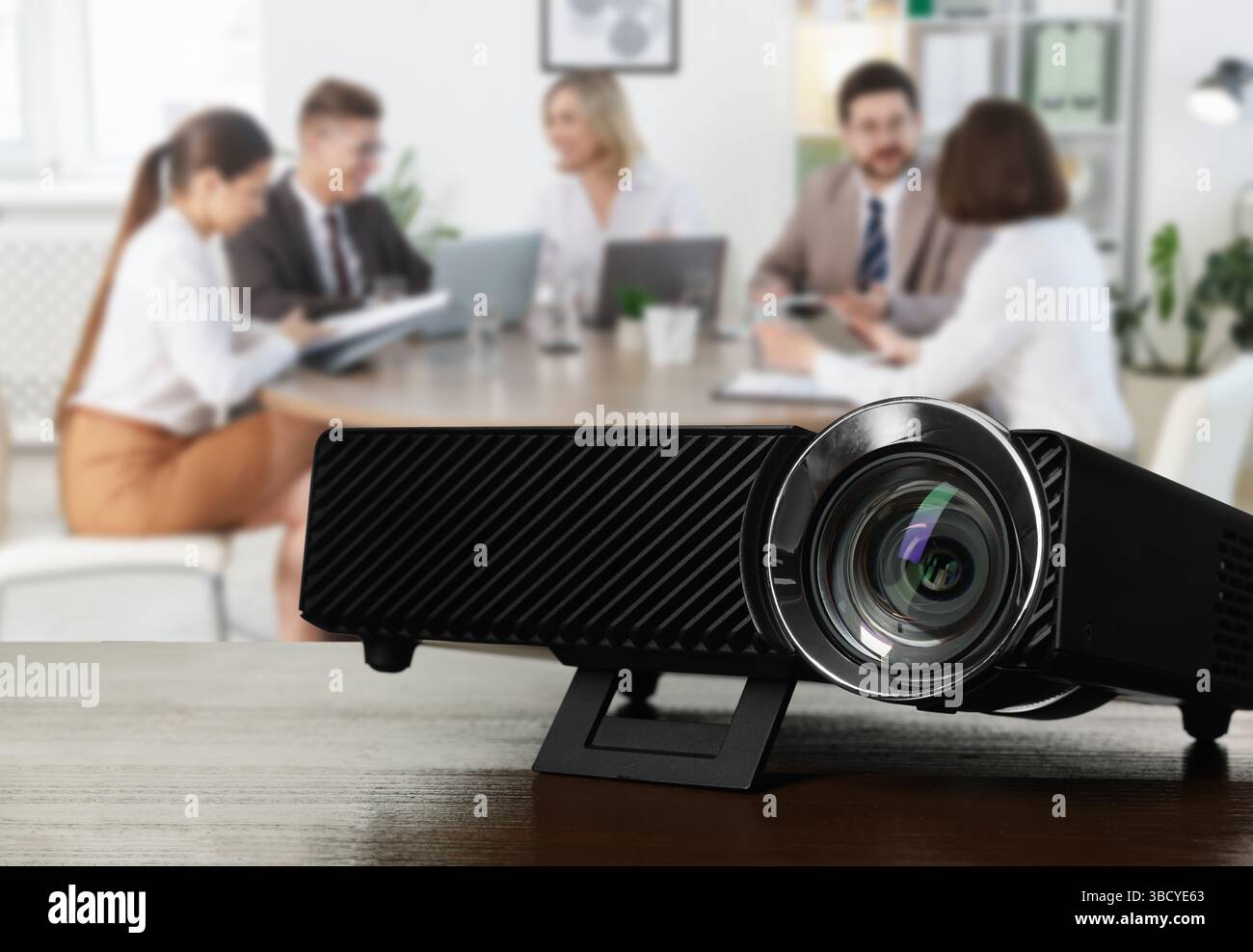 Moderner Videoprojektor auf Holztisch und Personen, die im Konferenzraum arbeiten, selektiver Fokus Stockfoto