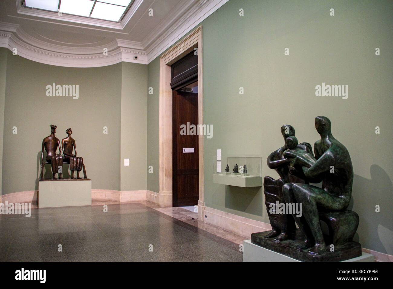 Moderne Bronzeskulpturen von Menschenfiguren und einer Familiengruppe, ausgestellt in einer ruhigen Museumsgalerie mit hellgrünen Wänden und Steinböden. Stockfoto