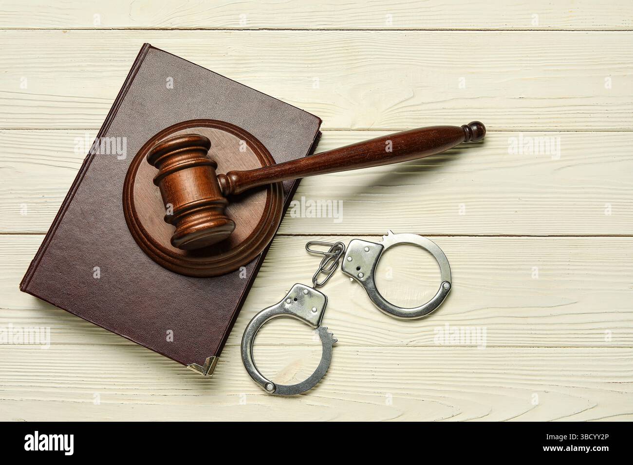 Handschellen mit Richtergabel und Gesetzbuch auf weißem hölzernem Hintergrund Stockfoto