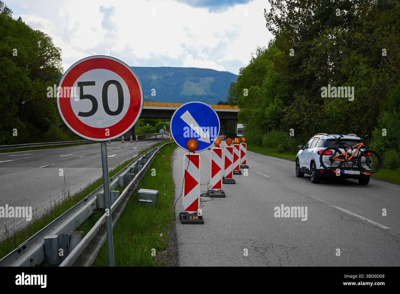 Straßenbaustelle mit einem Geschwindigkeitsbegrenzungsschild und einer Abweichung, bei der sich ein Fahrzeug nähert, Verkehrskegel und Warnleuchten. Stockfoto