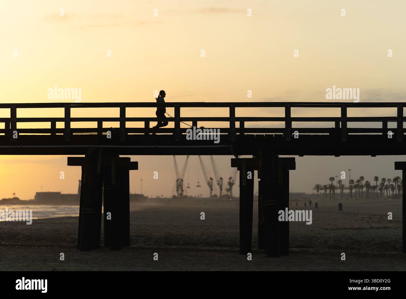 Frau joggt mit ihrem Hund am California Beach Pier bei Sunset Stockfoto