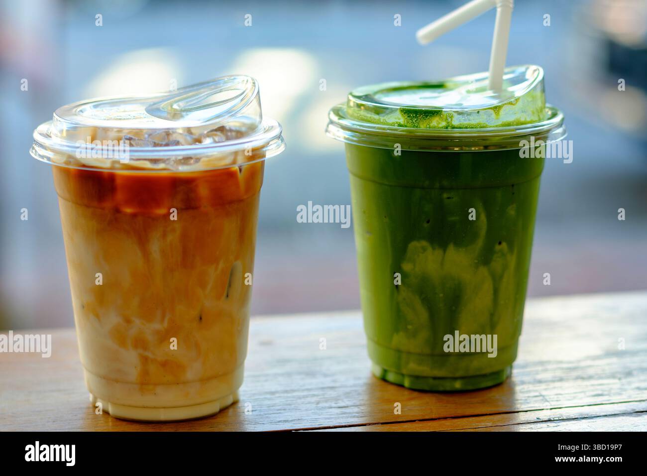 Ein warmes Bild von Eiskaffee und Matcha-Tee vor einem sonnendurchfluteten Café-Fenster, das entspannende Vibes, Café-Lifestyle und moderne Getränkekultur einfängt Stockfoto